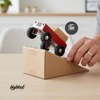 Small red wooden toy truck on a cardboard ramp with a hand initiating it, branded 'bigblock customs' and 'Tex'.