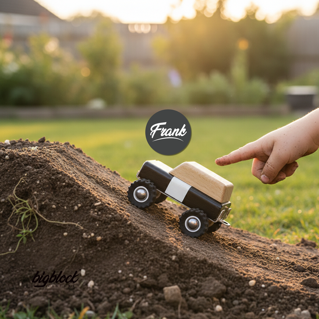 Wooden Toy truck with a block being pushed up a small hill by a hand in a park, with 'Frank' and 'bigblock' branding.