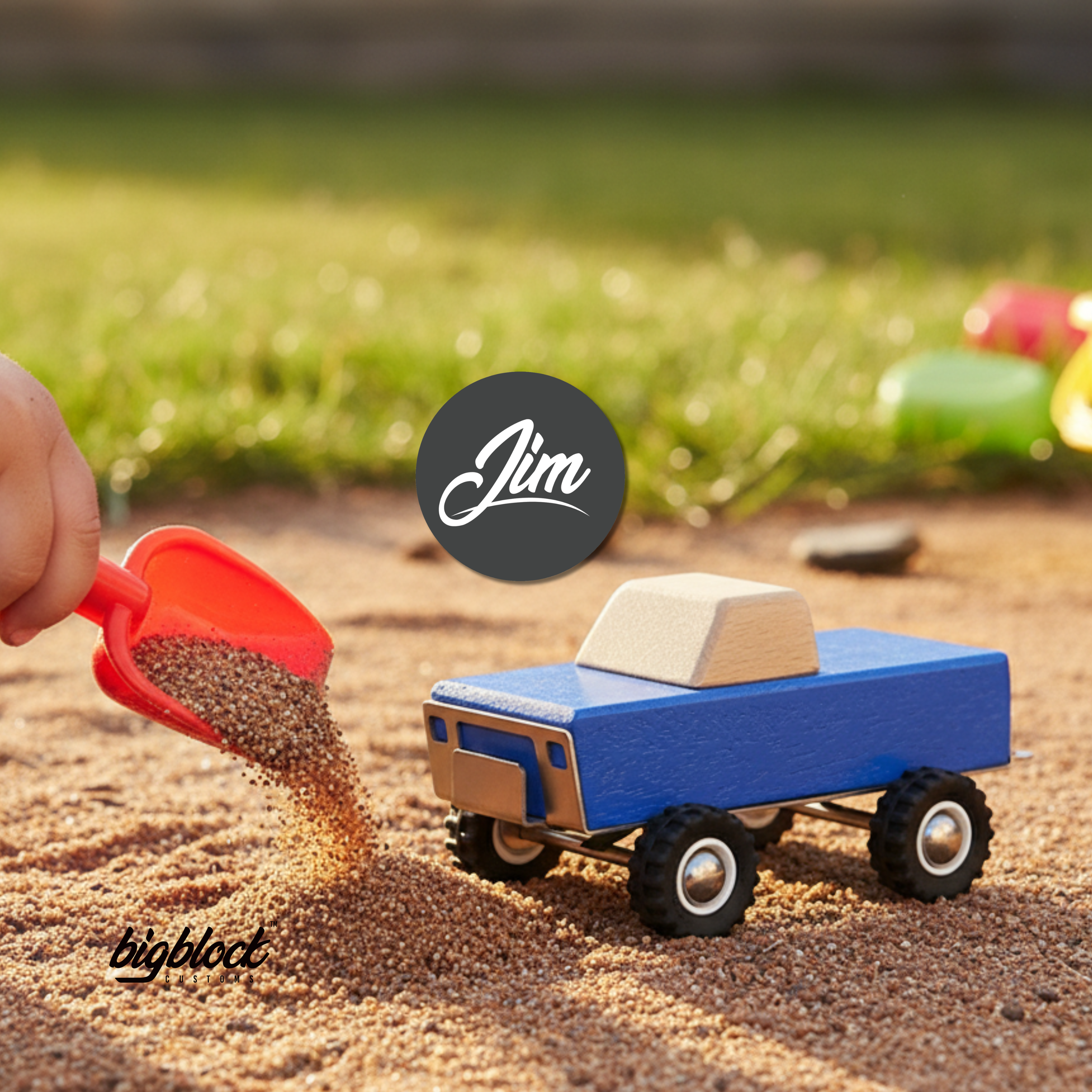 Blue Wooded Toy truck being filled with sand by a red shovel on a sandy surface, with 'Jim' and 'bigbloct' logos.