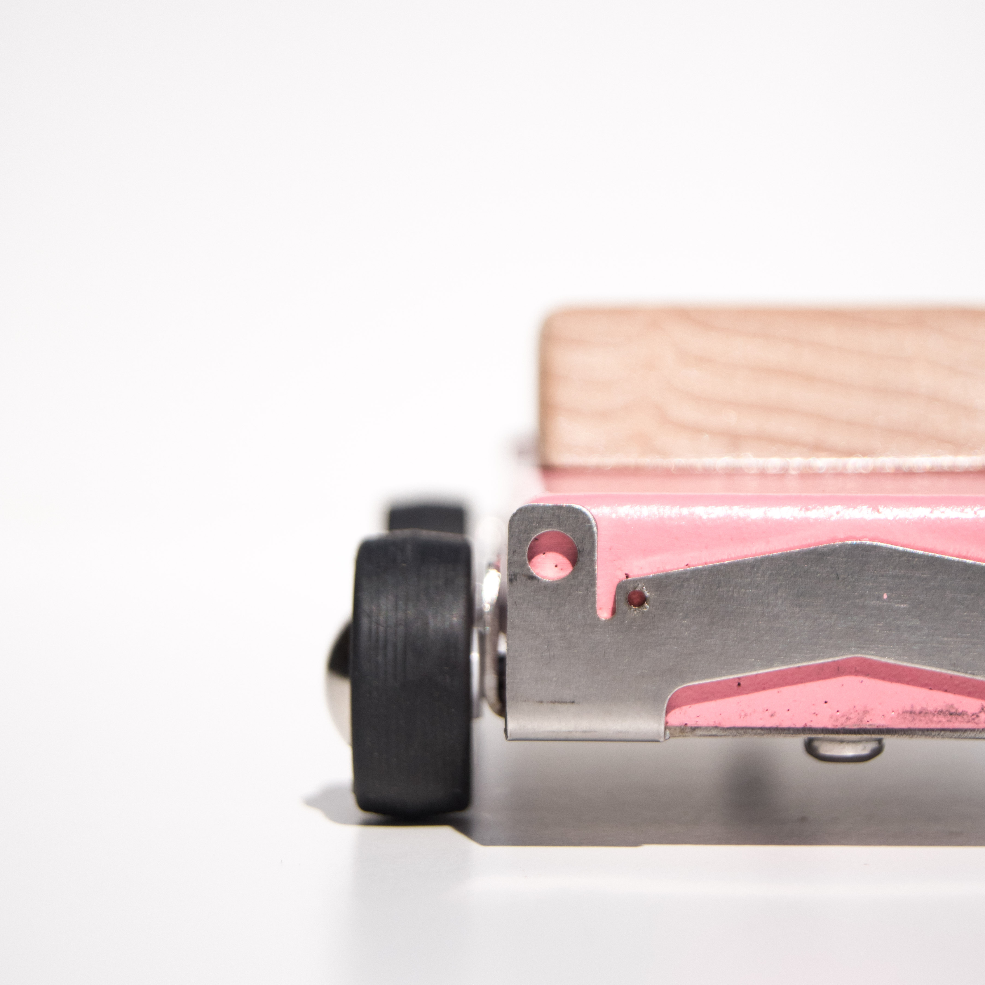 Close-up of a wooden toy car with pink color and black wheels on a white background