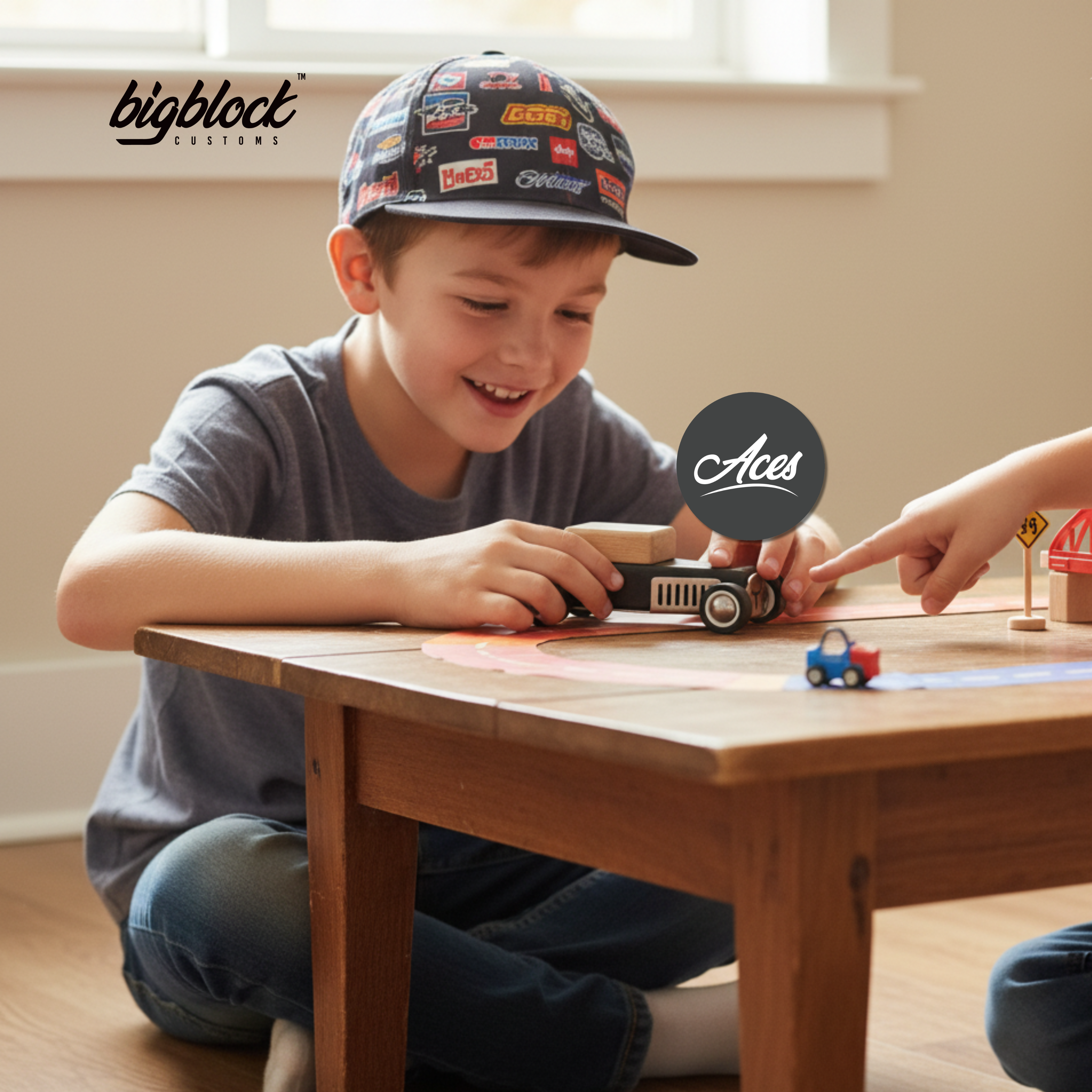 Child playing with wooden toycar at a wooden table, wearing a cap with brand logos.